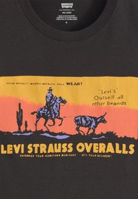 Cowboy på hest som kaster lasso på en storfe mot en solnedgang, med tekst som fremmer Levi Strauss bukser og merkevaren sin holdbarhet.