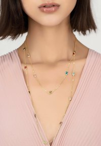 Gold layered necklace featuring various colorful rectangular gemstones and a delicate chain design, worn over a light pink top.