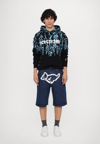 Black hoodie with blue lightning design and white "ice cream" text, paired with blue denim shorts featuring a white graphic. White sneakers and gray socks.