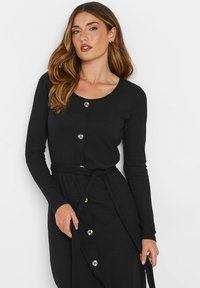 Robe noire à manches longues côtelées avec un col rond, des boutons sur le devant et une ceinture en tissu assorti nouée à la taille.
