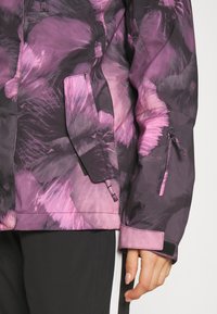 Water-resistant jacket in purple and black with a floral pattern, zippered pockets, and adjustable cuffs. Smooth texture and tailored fit.