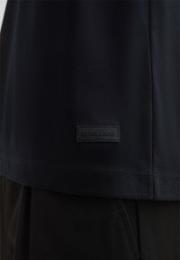 Czarna koszula z krótkim rękawem, wykonana z gładkiego materiału, z wyszywaną szwem i prostokątną czarną metką z wytłoczonym napisem "STRELLSON".