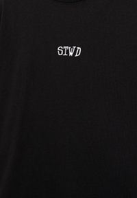 Tissu noir avec les lettres majuscules blanches "STWD" imprimées en petits caractères incurvés près du centre.