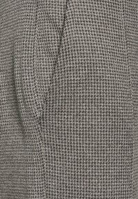 Texture de tissu tissé dans des nuances de gris présentant un motif pied-de-poule. Le matériau semble épais avec une surface douce et texturée.