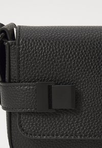 Borsa a mano in pelle nera testurizzata con forma rettangolare, delicata finitura a grana di ciottolo e chiusura a scatto nera opaca.