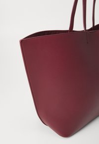 Burgundska torba od glatke kože s čvrstim dizajnom, koja ima dva dugačka remena i minimalističke šavove.