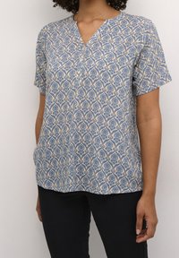 Kortærmet bluse i let stof, med et blåt blomster mønster på en beige baggrund, V-hals og knapdetalje ved kraven.