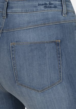 Blaue Jeans aus Denim mit einer Gesäßtasche, die gestickte Akzente und sichtbare Nähte aufweist. Der Stoff hat eine leicht ausgebleichte Textur.