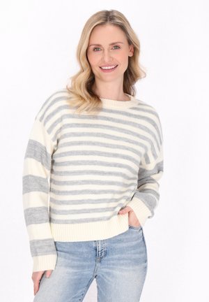 Maglione in maglia leggera con righe orizzontali grigie e crema, scollatura ampia e polsini a coste. Abbinato a jeans azzurri chiari.