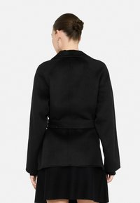 Abrigo de lana negra con cintura ceñida, con cuello de muesca y mangas largas. Textura suave con un ajuste entallado y estructurado.