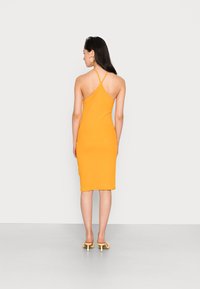Vestido midi ajustado laranja, com design de alça nadador, textura suave e alças finas. Usado com mules amarelos de salto. Vista traseira apresentada.