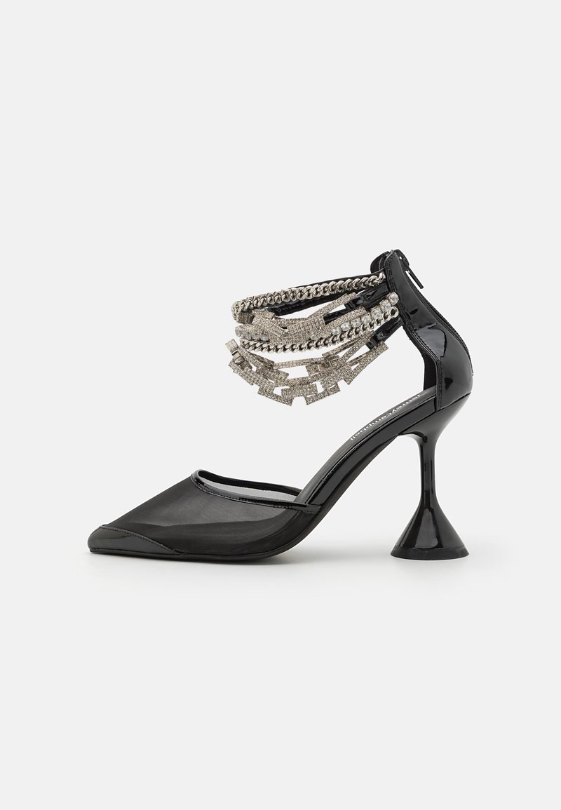 Escarpin en cuir verni noir avec un bout pointu, doté d'un talon conique et d'un détail décoratif en chaîne métallique sur la bride de cheville.