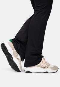 Sneaker chunky beige e bianche con tomaia in mesh testurizzata e suola nera. Presentano un accento verde sul tallone e sui lacci.