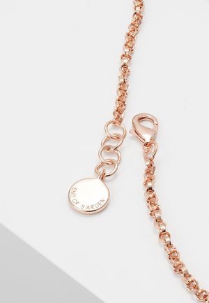 Collana con catena in oro rosa con chiusura a moschettone e una piccola medaglia rotonda incisa con "SNÖ OF SWEDEN" su sfondo bianco.