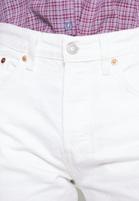 Pantalones vaqueros de denim blanco con un diseño clásico de cinco bolsillos, herrajes metálicos y remaches de cobre. La textura parece suave con un ajuste ligeramente estructurado.