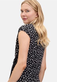 Sort top med korte ærmer, der har et hvidt prikmønster. Stoffet ser glat ud med en afslappet pasform og subtil drapering.