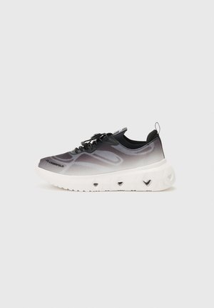 Zapatilla moderna negra y gris con suela blanca y gruesa con recortes en forma de corazón y lengüeta en el talón, sobre un fondo liso.