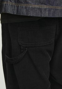 Zwarte corduroy broek met een gestructureerd ribbelpatroon, voorzien van een zijzak en een iets ontspannen pasvorm. Geaccentueerd met een contrasterende naad.