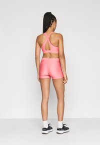 Ροζ αθλητικό σουτιέν με σχεδιασμό σταυρωτής πλάτης και λεπτομέρεια λογότυπου, συνδυασμένο με ταιριαστό σορτς. Ομαλή υφή υφάσματος με εφαρμοστή σιλουέτα.