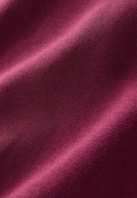 Bordeauxfarbener Baumwollstoff mit einer glatten Textur, der über einen subtilen Stretch und ein feines Strickmuster verfügt und sanft über die Oberfläche fällt.