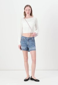 Suéter corto blanco de punto con mangas largas, combinado con pantalones cortos de mezclilla azul claro. Bailarinas negras y un pequeño bolso de hombro completan el atuendo.