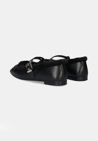 Bailarinas de cuero negro con punta redondeada, con un ribete de pelo sintético, dos correas ajustables con herrajes plateados y una suela plana.