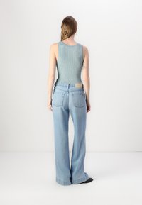 Jean large de couleur bleu clair, à taille haute, associé à un débardeur ajusté en maille de couleur vert menthe. Le tissu a une texture lisse et peu de détails.