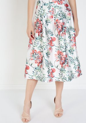 Falda midi floral en blanco, con vibrantes estampados botánicos en rojo y verde. Diseño plisado con una textura de tela ligera y fluida.