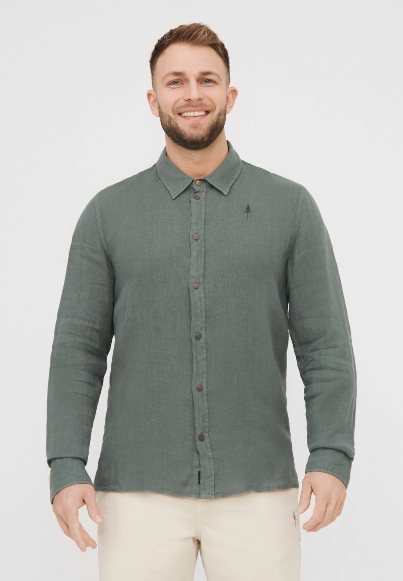 Camicia verde con bottoni, realizzata in tessuto testurizzato, con colletto, bottoni in legno e un piccolo ricamo di un albero sul petto.