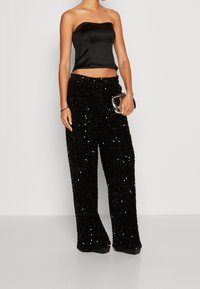Zwarte satijnen strapless crop top gecombineerd met loszittende zwarte paillettenbroek, met een gladde textuur en een glanzend, reflecterend oppervlak.