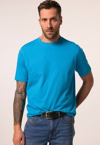 T-shirt di cotone turchese con maniche corte, scollatura rotonda e vestibilità rilassata, abbinata a jeans denim blu e una cintura nera.