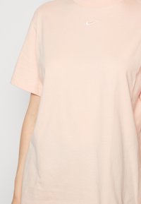 Light pink short-sleeve T-shirt worn by a person, featuring a small white Nike swoosh logo centered below the neckline.