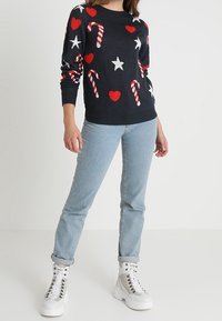 Marinblå tröja med röda hjärtan, vita stjärnor och röd-vita randiga polkagrisar. Kombinerad med ljusblå jeans och robusta vita stövlar.