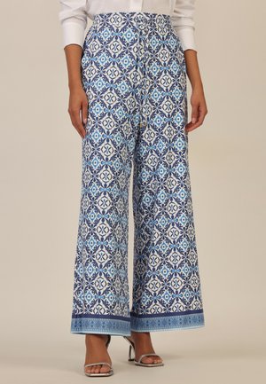 Weit geschnittene Hosen mit blau-weißen geometrischen und floralen Fliesenmustern, mit einem Kordelzug am Bund, kombiniert mit silbernen offenen High-Heels.