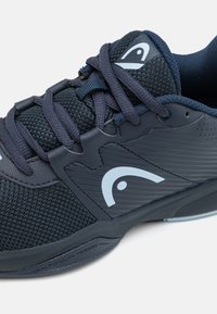 Mörkblå atletiska skor med mesh-överkonstruktion, gummisula och en framträdande logotyp. Har snörningsdesign och texturerade överläggsdetaljer.