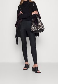 Suéter de cuello alto negro, poncho con acentos en negro y púrpura, jeans oscuros, sandalias de tacón cuadrado negras y un bolso tejido en blanco y negro.