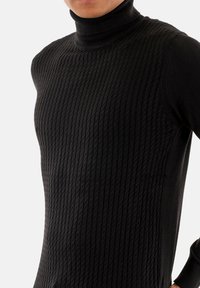 Maglione nero a collo alto con texture a coste, caratterizzato da un design aderente e un tessuto liscio, che mostra un sottile motivo verticale.
