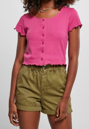 Mujer con una camiseta rosa de manga corta abotonada y top corto, y pantalones cortos de talle alto verde oliva con dobladillo enrollado.