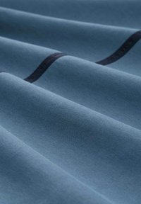 Niebieski materiał o gładkiej teksturze, z subtelnymi fałdami i ciemnym poziomym paskiem na tle.