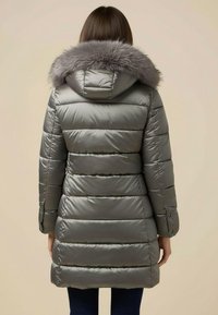 Stříbrná prošívaná bunda typu puffer s kapucí z umělé kožešiny, prošívaným designem a dlouhými rukávy. Má manžety na knoflíky a středně dlouhý střih.