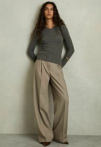Šedý fitted top s dlouhým rukávem a texturovaným vzorem, kombinovaný s béžovými širokými kalhotami a hnědými špičatými podpatky na neutrálním pozadí.