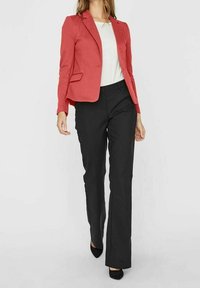 Korallinvärinen bleiseri, jossa on muotoiltu istuvuus ja kaksi etutaskua, yhdistetty mustiin muotoiltuihin housuihin ja mustiin korkokenkiin. Valkoinen aluspaita näkyvissä.