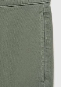 Gros plan sur un tissu vert kaki avec une armure diagonale et des coutures renforcées le long d'une couture verticale et d'un bord horizontal.