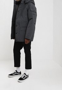 Szara kurtka ocieplana z kapturem, z wieloma kieszeniami i zapięciem na napy. Połączona z czarnymi spodniami 3/4 i czarno-białymi sneakersami.