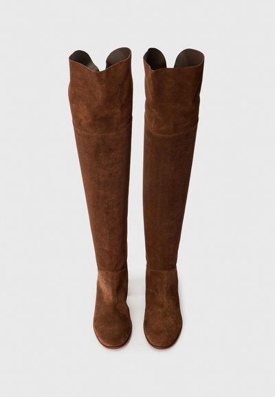 Botas marrones de ante hasta la rodilla con una textura suave, que presentan un diseño holgado y punta afilada. Sin herrajes ni patrones visibles.