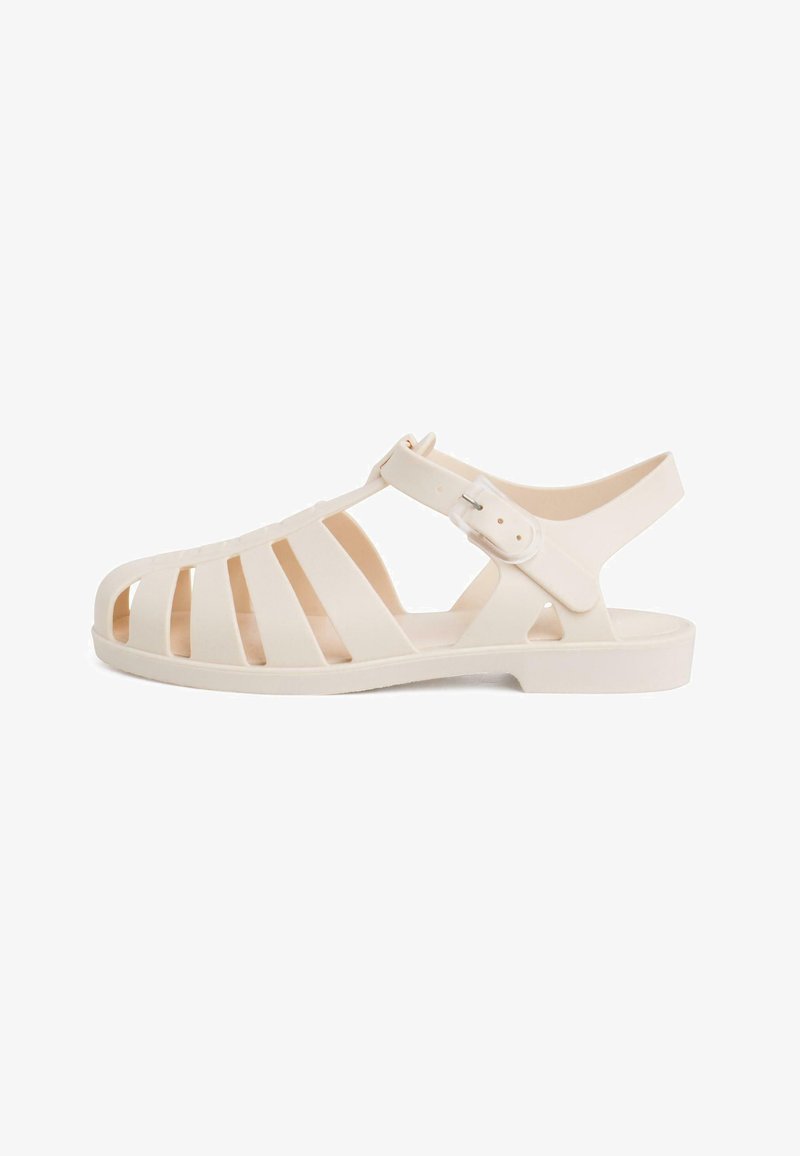 White rubber sandal with multiple vertical cutouts, adjustable buckle strap, and flat sole. Designed for breathability and easy wear.