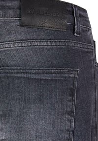 Sötétszürke farmernadrág sima textúrával, fekete bőr folttal a deréknál és standard hátsó zsebekkel.