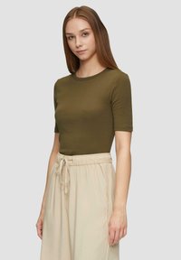 Olivengroen slim fit t-shirt met een ronde hals en korte mouwen, gecombineerd met lichtbeige, broek met drawstring taille en wijde pijpen.