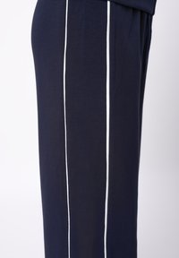 Joggers bleu marine avec des bandes blanches sur les côtés, fabriqués en tissu doux. Ils disposent d'une taille élastique et d'une poche zippée sur le côté.