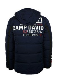 Chaqueta acolchada color azul marino con capucha, presenta un gran texto en blanco y rojo "CAMP DAVID" y coordenadas geográficas, superficie texturizada y detalles en negro.
